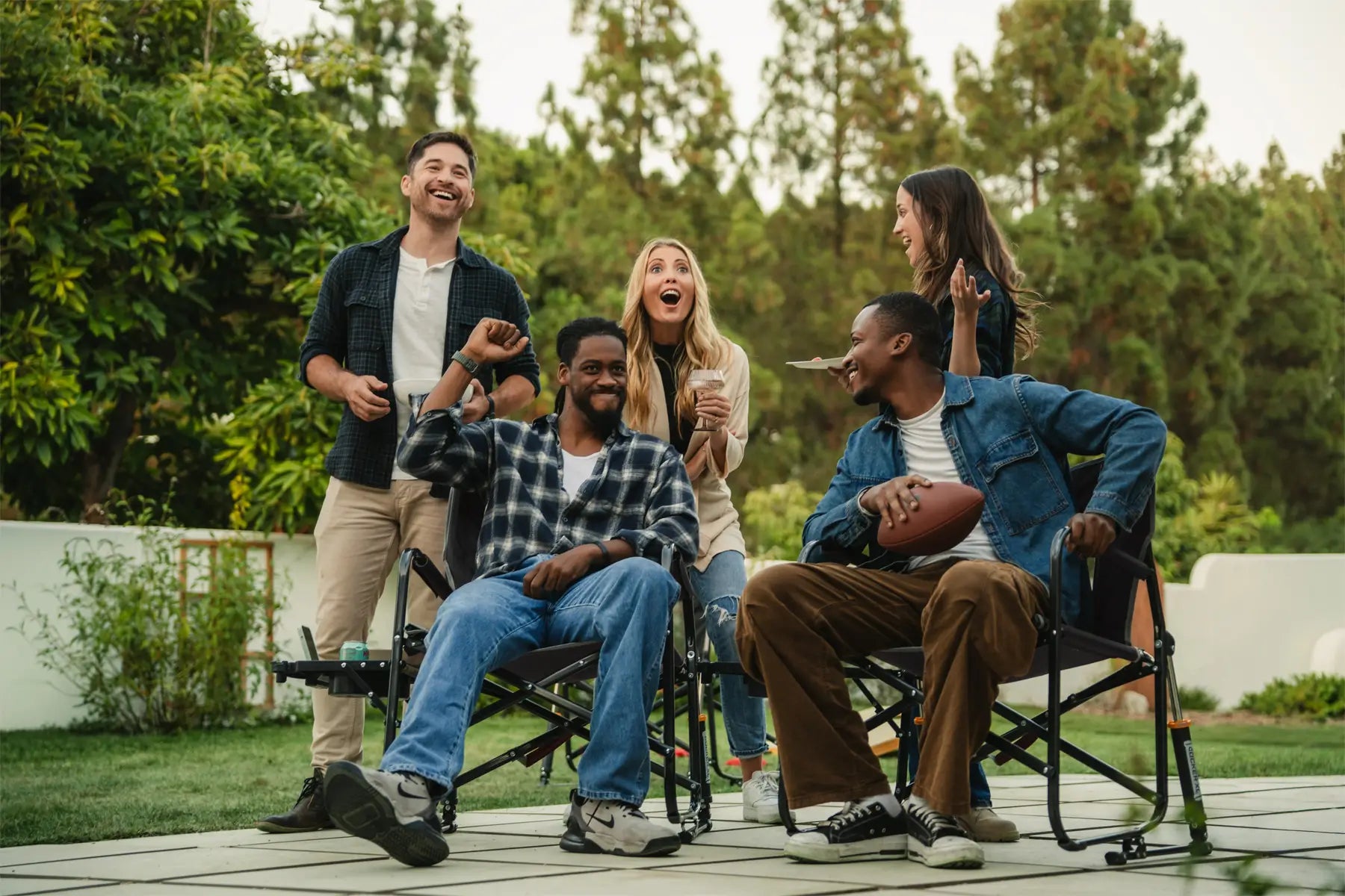 A group of people cheering in a backyard setting while two people sit in gci outdoor chairs. 