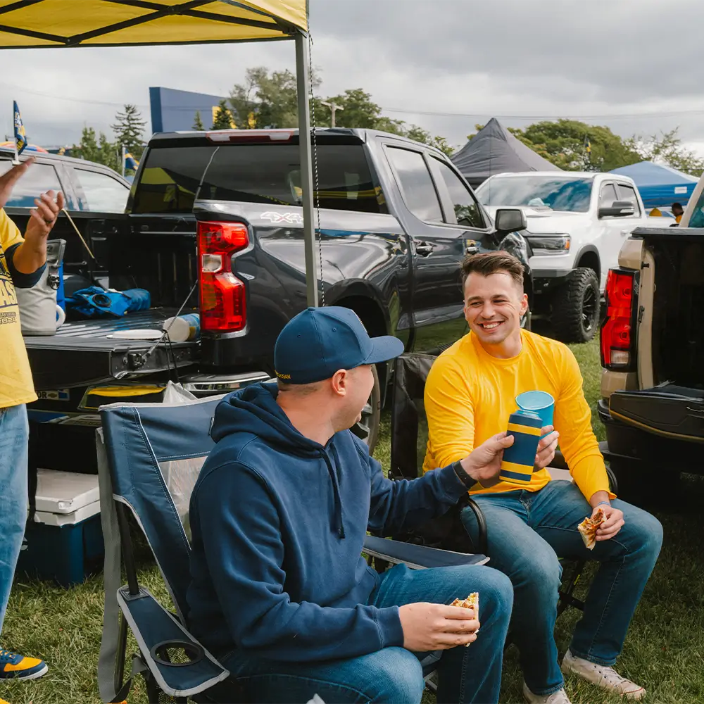 Two men sitting near a group of tailgaters while they talk in their stowaway and comfort pro rocker. 