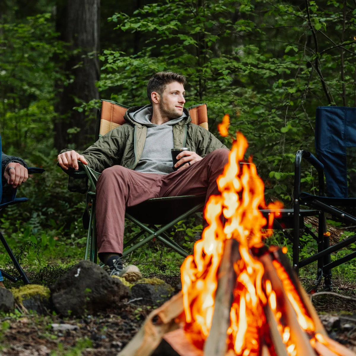 A man sitting in an Insulated Comfort Pro Rocker while sitting next to a bonfire. 