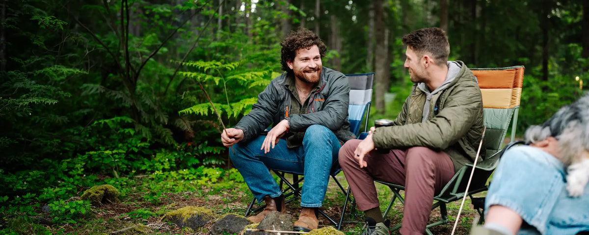 Two men sitting by a bonfire while sitting in two Insulated Comfort Pro Rockers. 