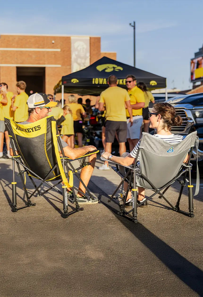 A couple sitting in iowa state comfort pro rocker chairs, that say hawkeyes on the back while hanging out at a tailgate. 