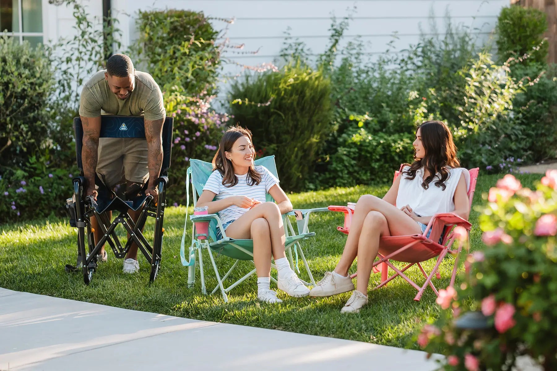 Two women sitting in pastel colored Kickback Rockers while talking in a backyard setting. 