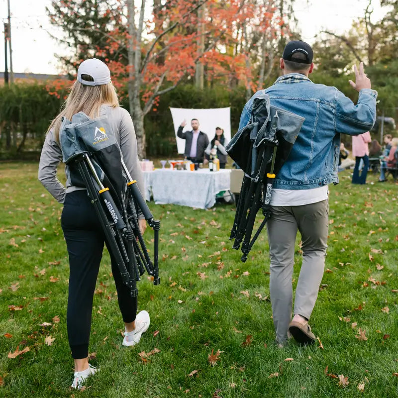 Couple walking to an outdoor event carrying folded heathered pewter Kickback Rockers.