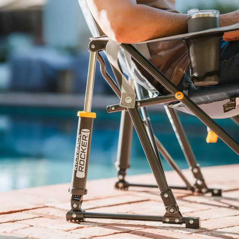 Close-up of the heathered pewter Kickback Rocker showing spring action rocking technology and cup holder by a poolside patio.