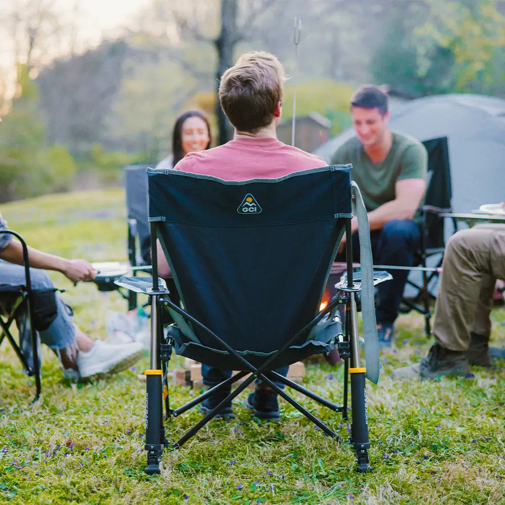 A man sitting in an indigo kickback rocker chair next to people gathered around a fire. 