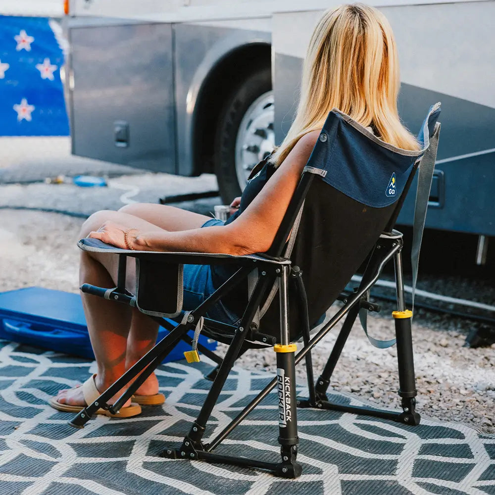 A woman sitting in an indigo kickback rocker chair next to an rv. 