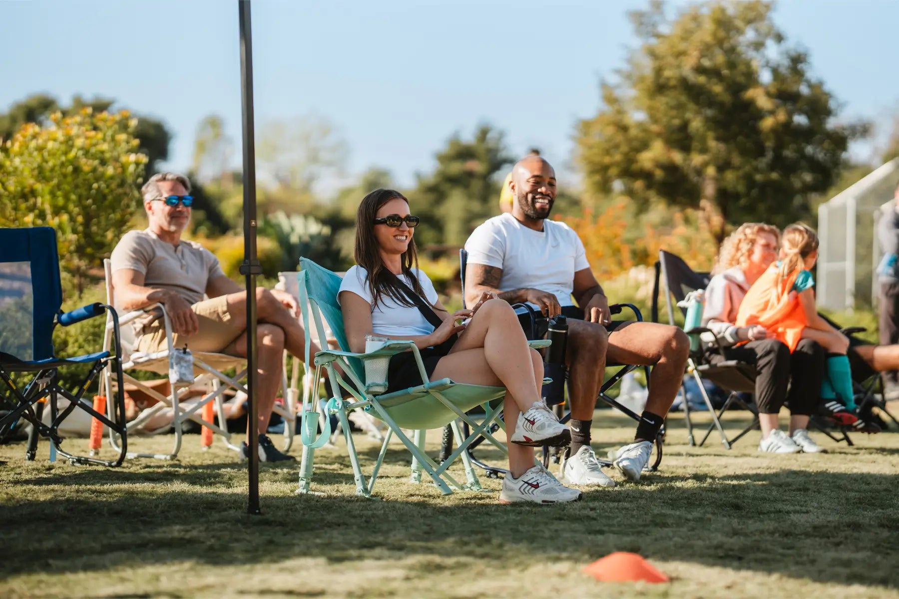 Couple sitting in GCI Kickback Rockers at a sports field, smiling and holding drinks.