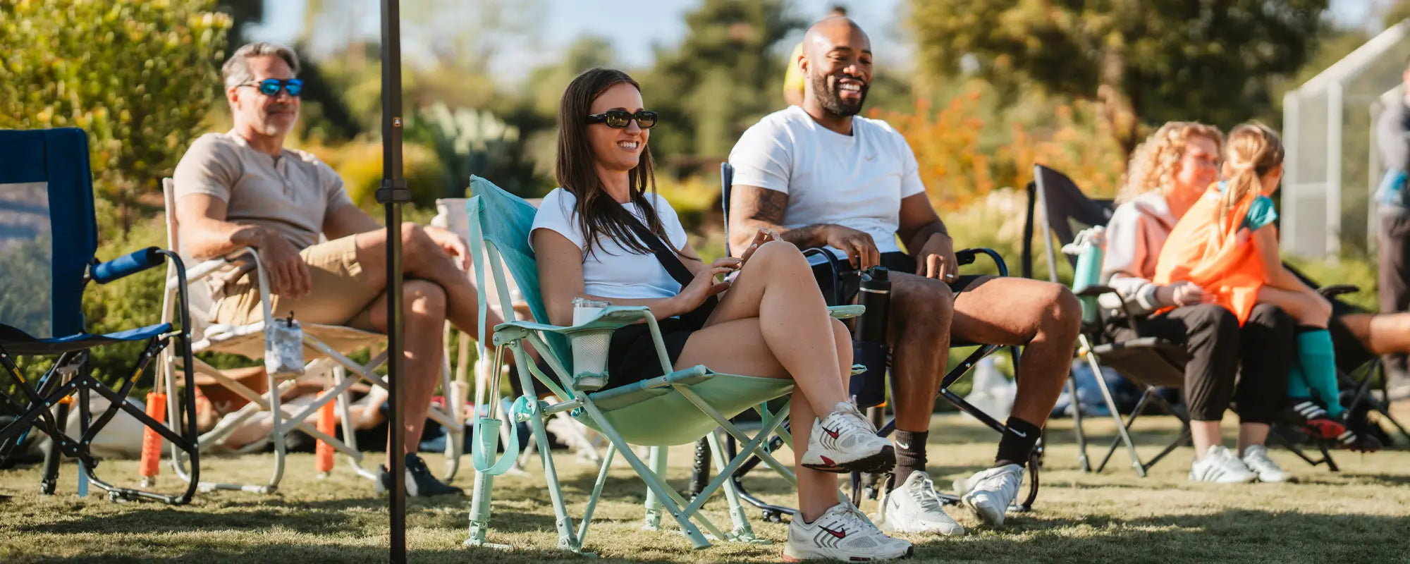 Couple sitting in GCI Kickback Rockers at a sports field, smiling and holding drinks.