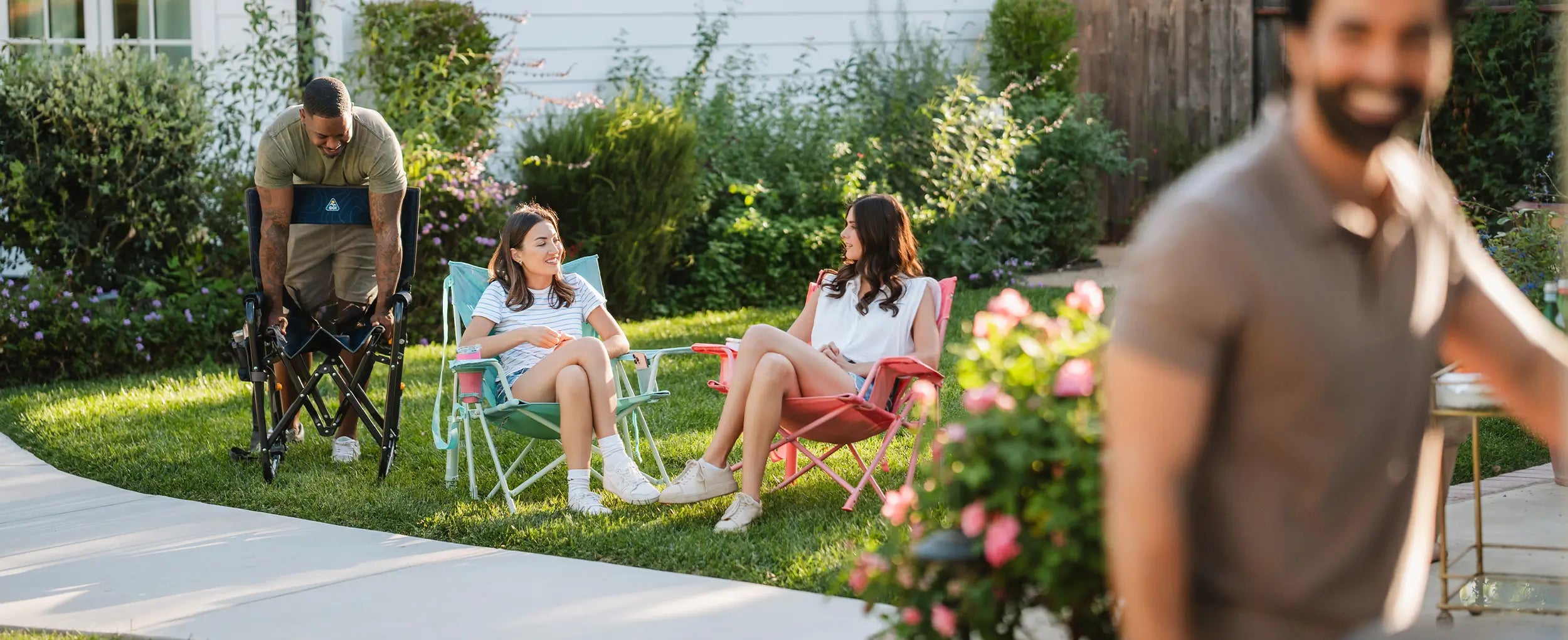 Two women sitting in pastel colored Kickback Rockers while talking in a backyard setting. 