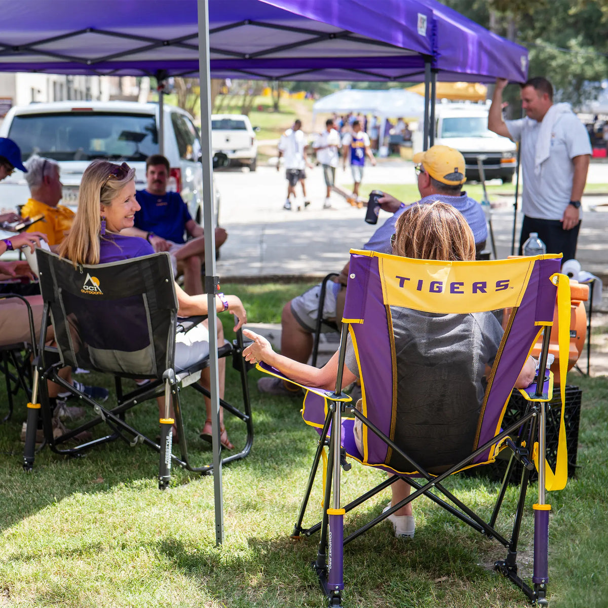 A woman sitting in an LSU comfort pro rocker chair while chatting with a group of tailgaters sitting under a canopy. 