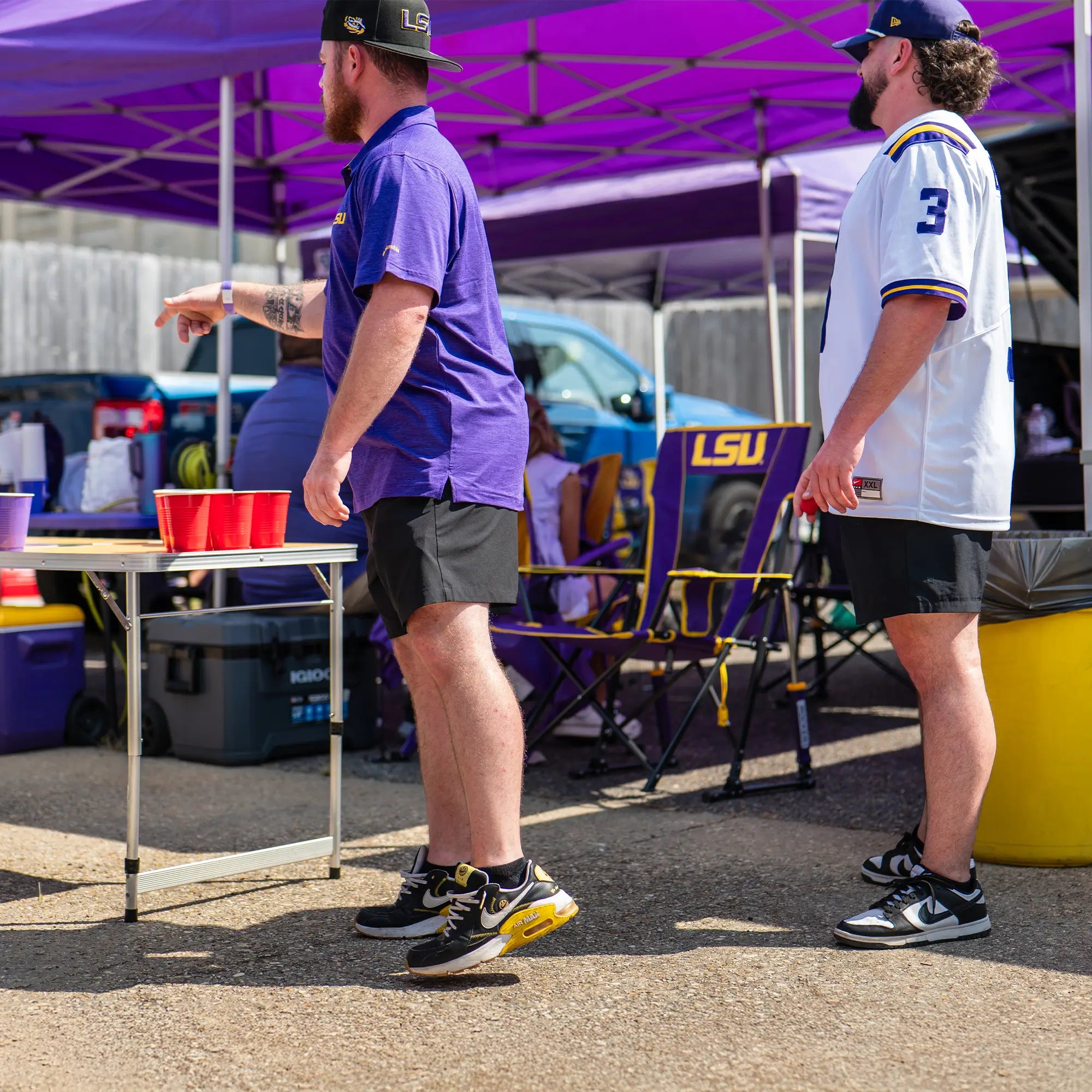 Two men throwing ping pong balls at cups while standing next to an LSU comfort pro rocker chair. 
