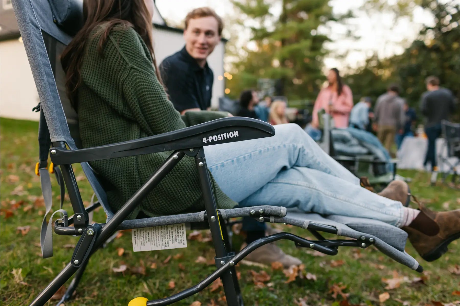 A woman reclines in a Legz Up Lounger at an outdoor gathering, emphasizing its comfort and elevated leg support.