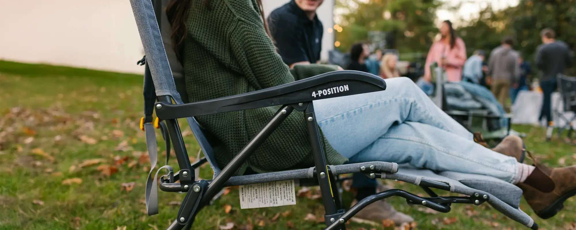 A woman reclines in a Legz Up Lounger at an outdoor gathering, emphasizing its comfort and elevated leg support.