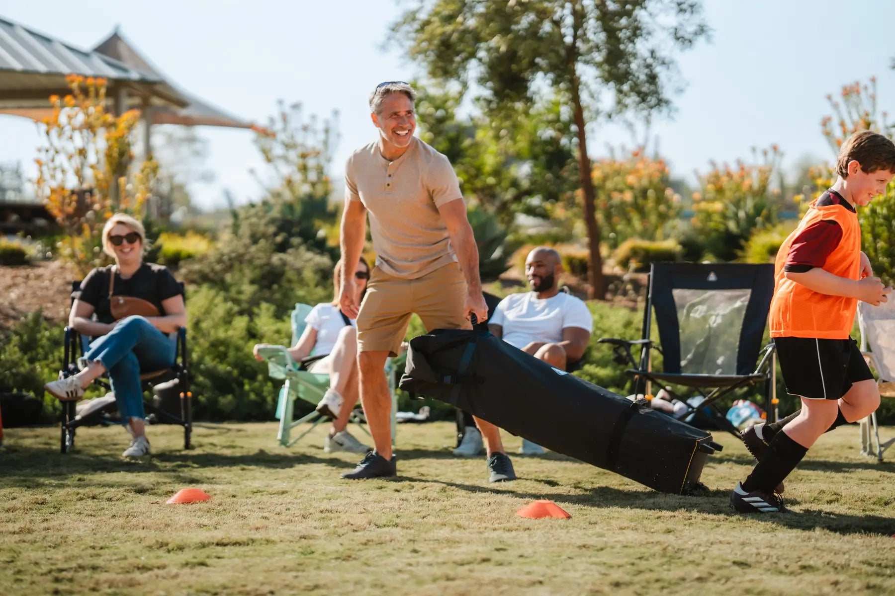 A man sets up a Levrup Canopy at a soccer field, providing quick shade for spectators watching the game.