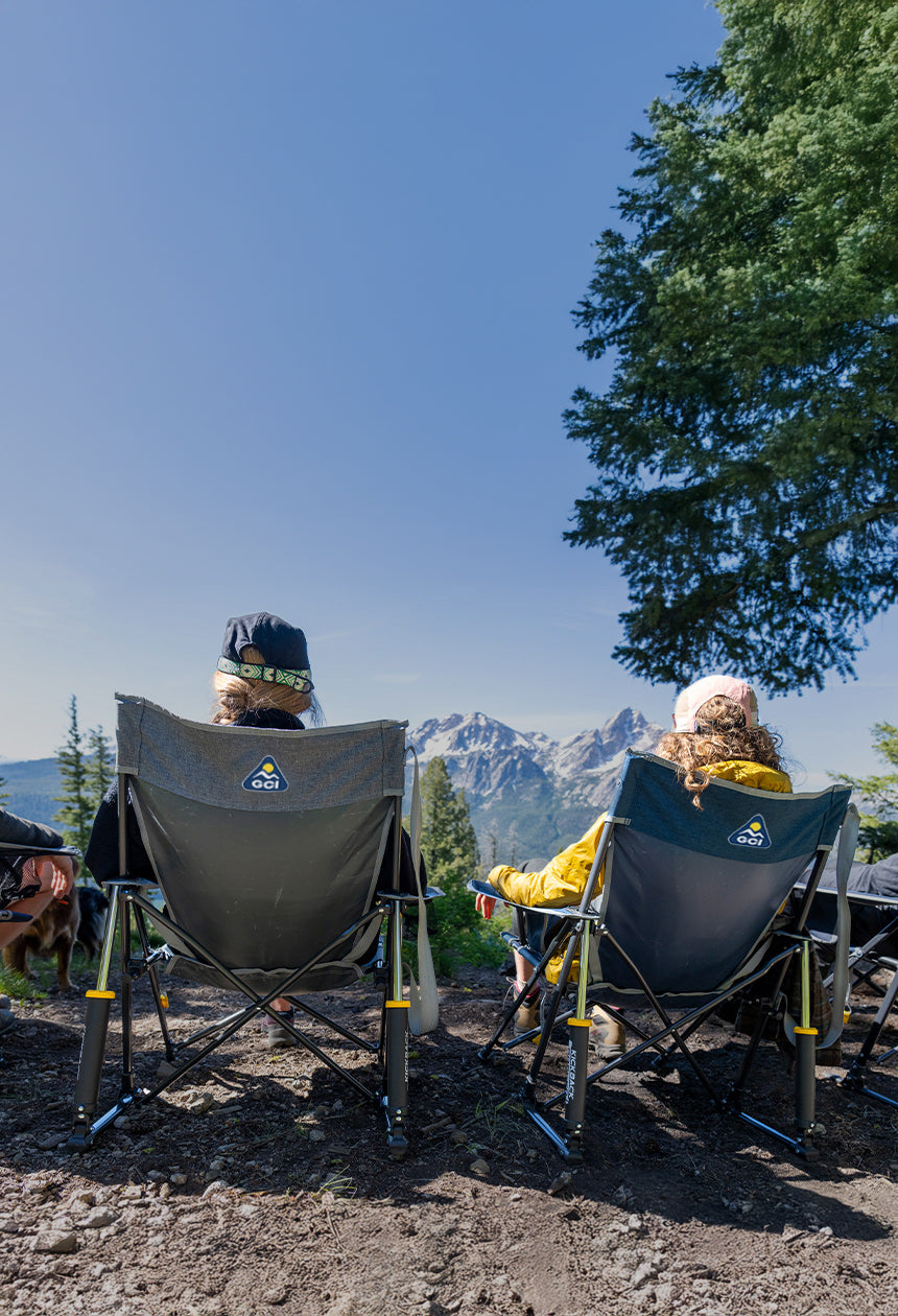 Two women sitting in a comfort pro rocker chair on a cliff overlooking a mountain. 