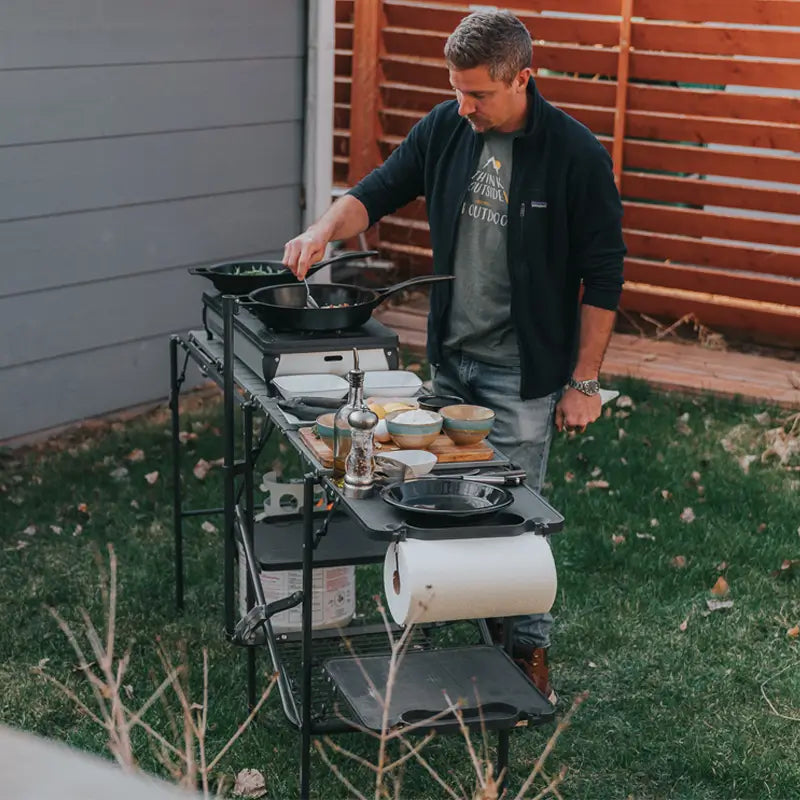 Man cooking with cast iron on a Master Cook Station, fully set with dishes, utensils, and a roll of paper towels.