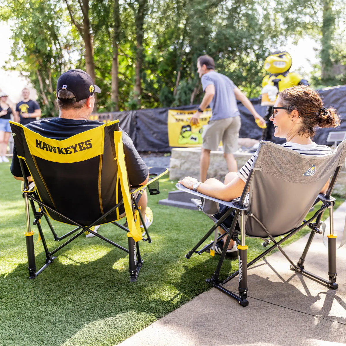 A couple sitting in iowa state comfort pro rocker chairs watching a group play cornhole. 