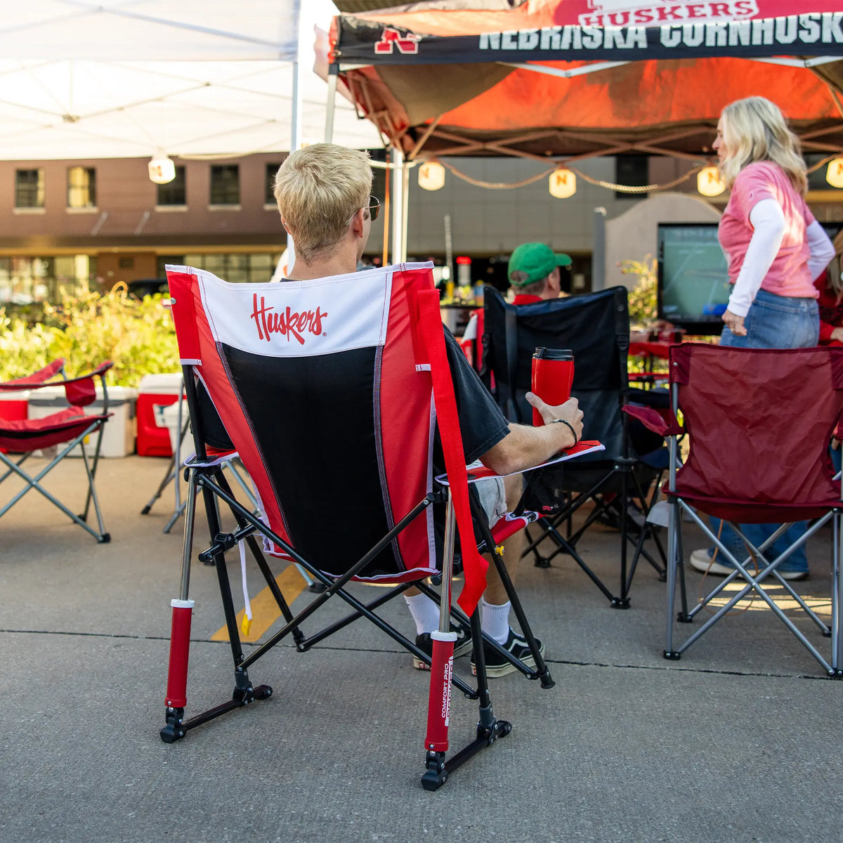 A man watching a football game on tv while sitting in a nebrask huskers comfort pro rocker. 