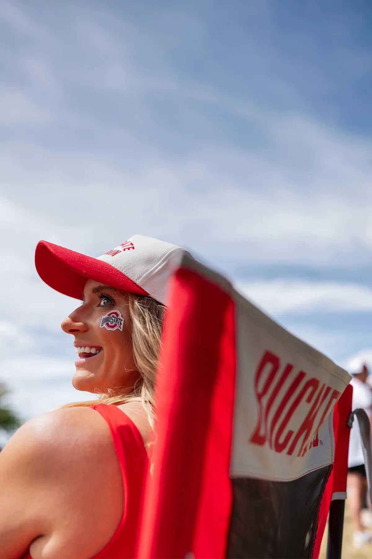 A woman sitting in an Ohio State Buckeyes chair while attending a tailgate party. 