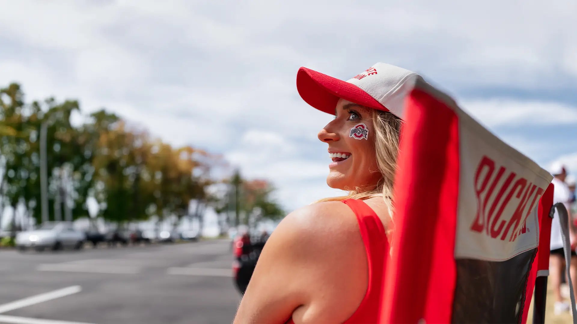 A woman sitting in an Ohio State Buckeyes chair while attending a tailgate party. 