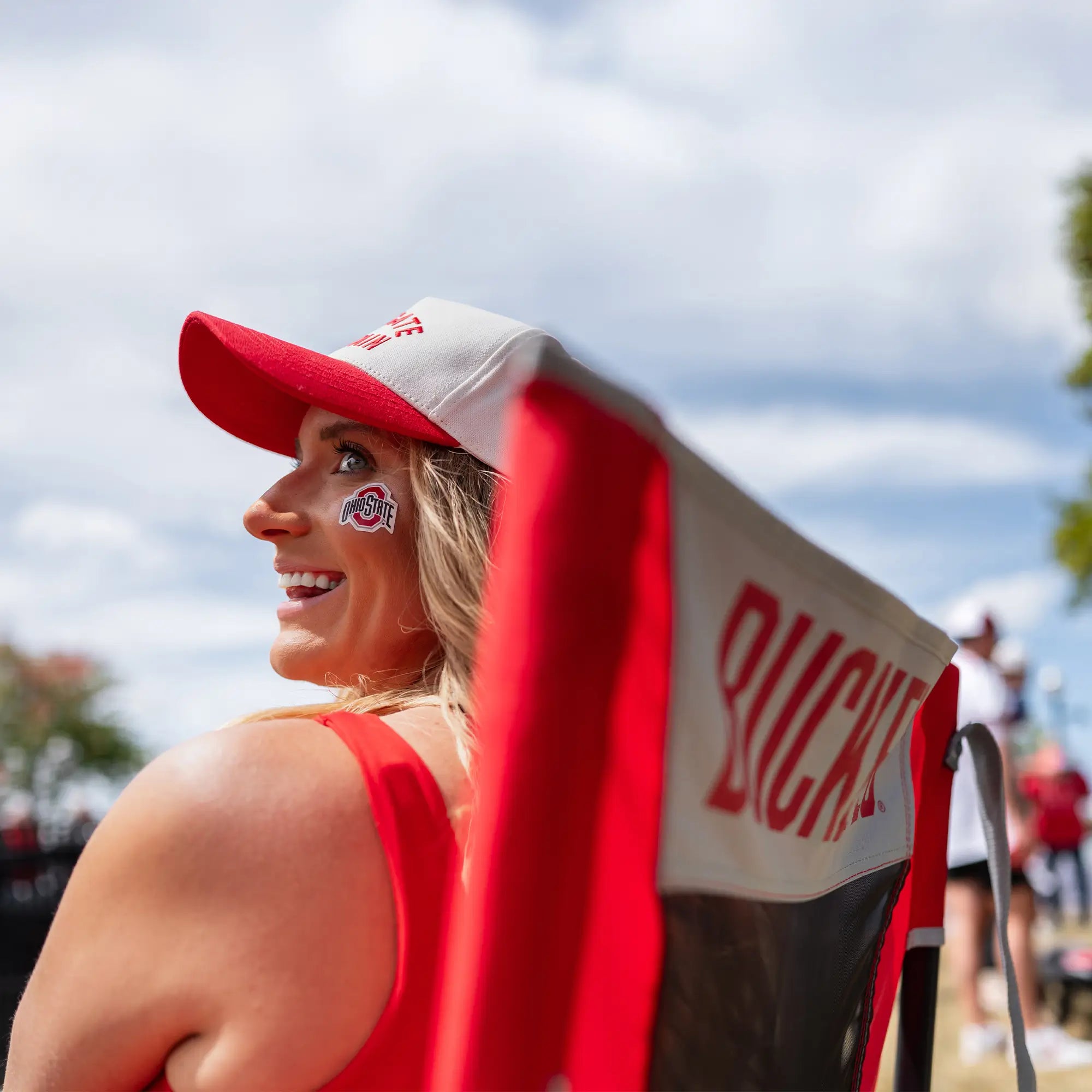 A tailgater smiling and conversing with someone while sitting in an ohio state buckeyes comfort pro rocker. 