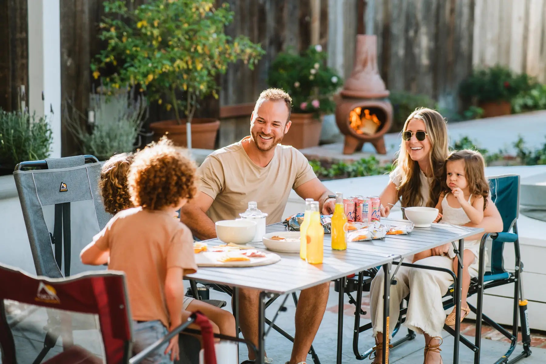 Family sitting at the slim-fold table in their backyard eating together. 