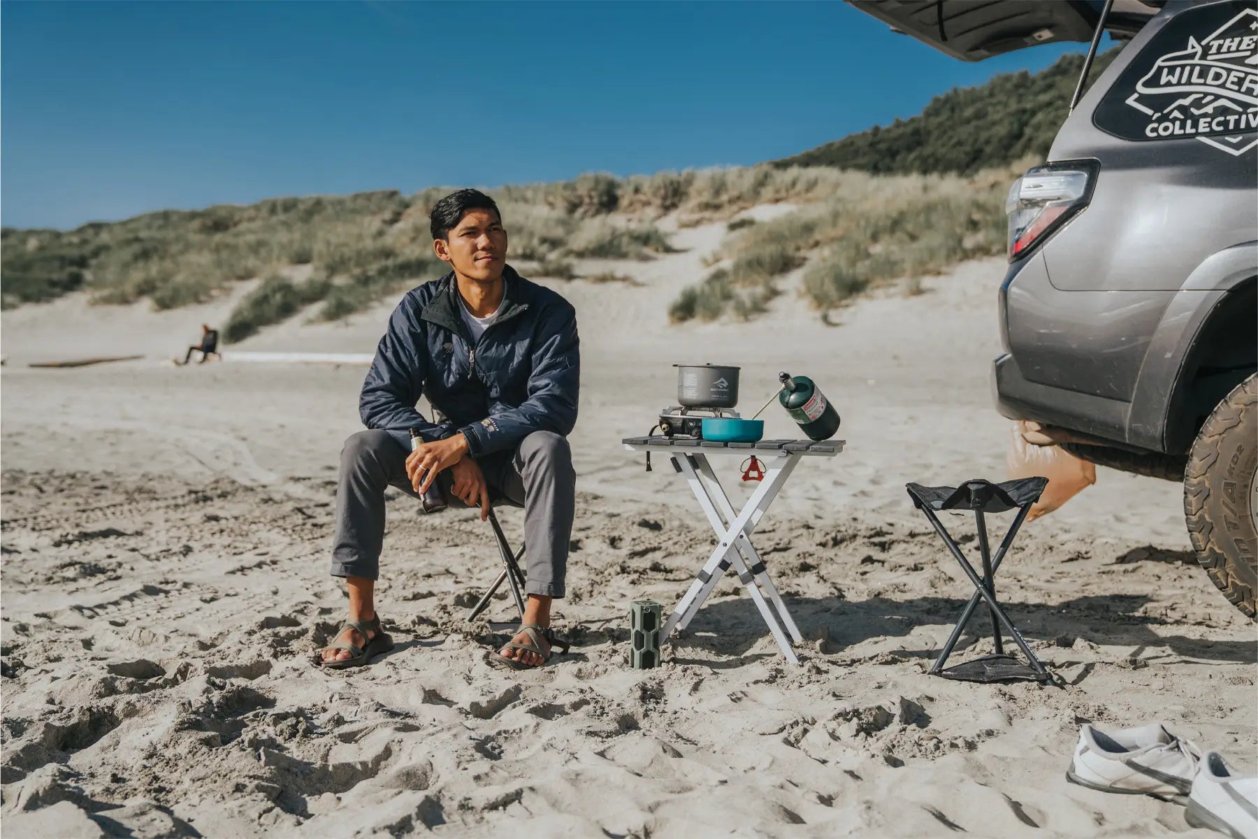 Man sitting on a Packseat on a sandy beach next to a small table with cooking gear.