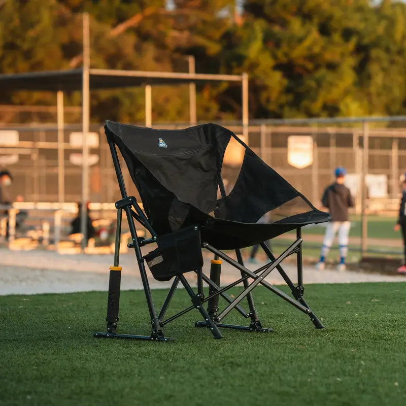 Pod Rocker chair set on grass near a baseball field, angled to show its supportive sling seat and spring-action frame.