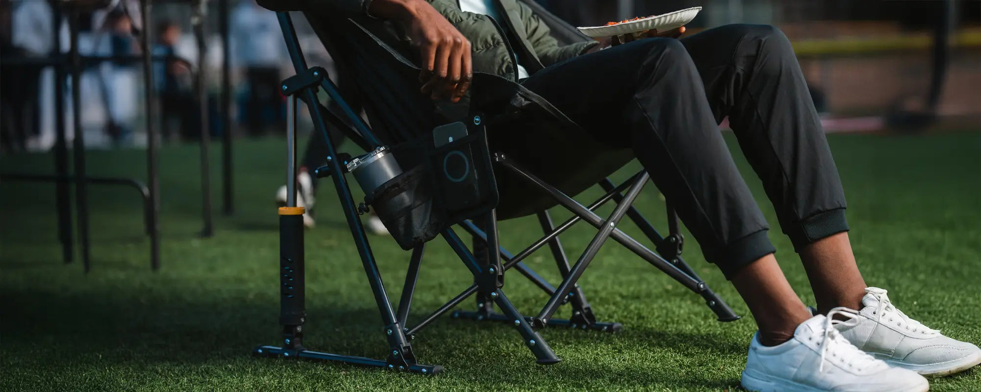 Person sitting in a Pod Rocker at a sporting event, holding a plate of food with a cup holder attached.