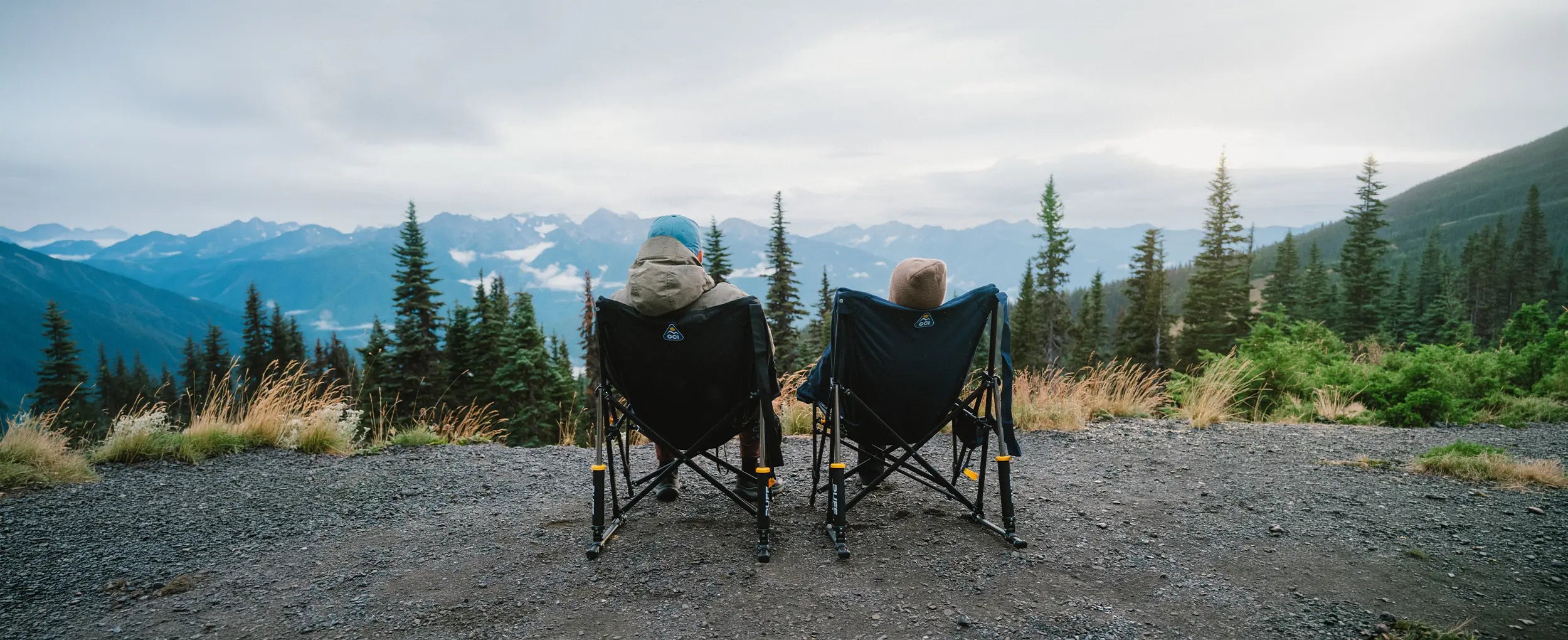 A couple observing a mountainous overlook while sitting in two Puff Rocker chairs. 