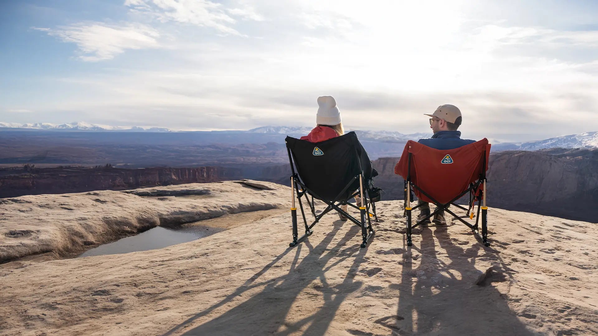 A couple sitting near a mountain cliff taking in the view on their puff rocker chairs. 