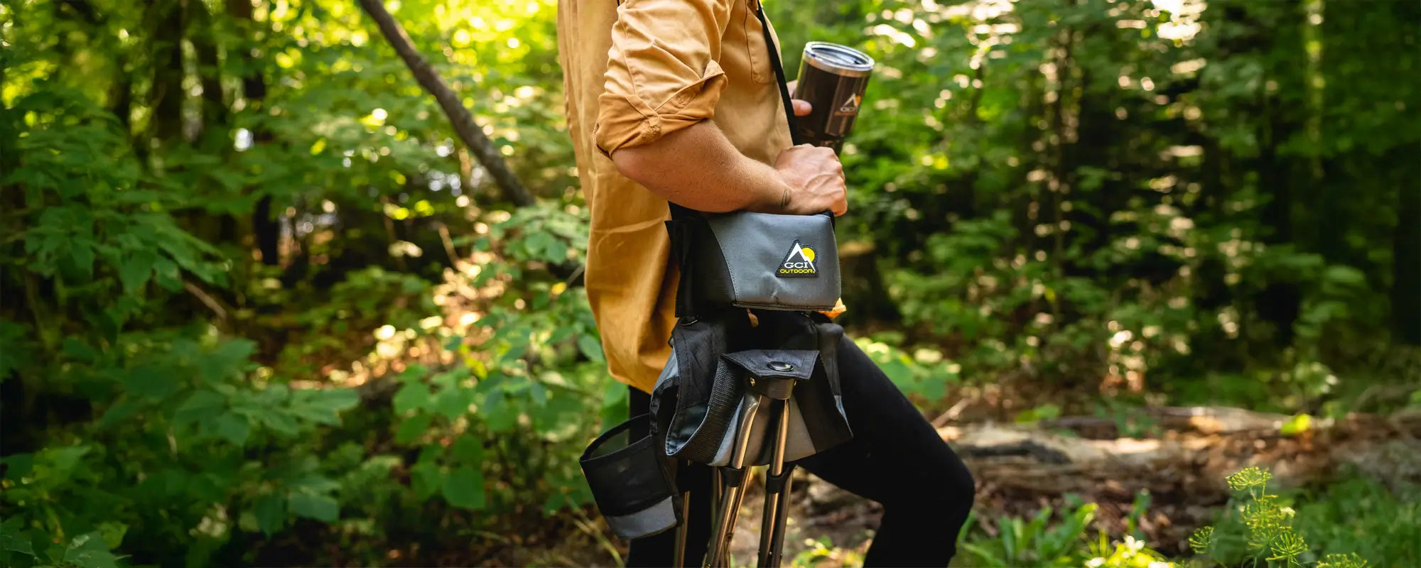 Person carrying a Quik-E-Seat through a forest, holding a branded travel mug.