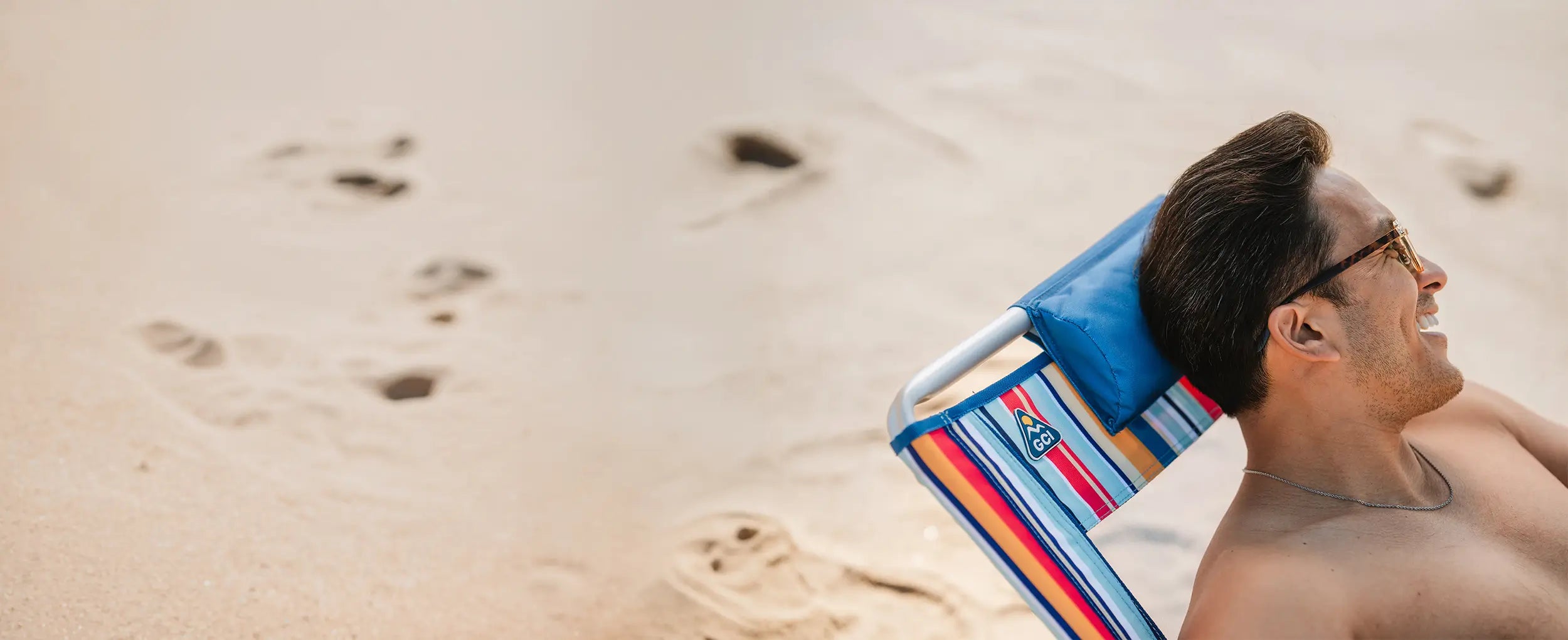 A shirtless man reclined back on a multi stripe Backpack Beach Chair on a beach. 