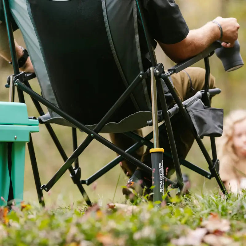 Close-up of the RoadTrip Rocker in mercury gray from behind, showing spring-action shocks and storage pocket on grassy ground.