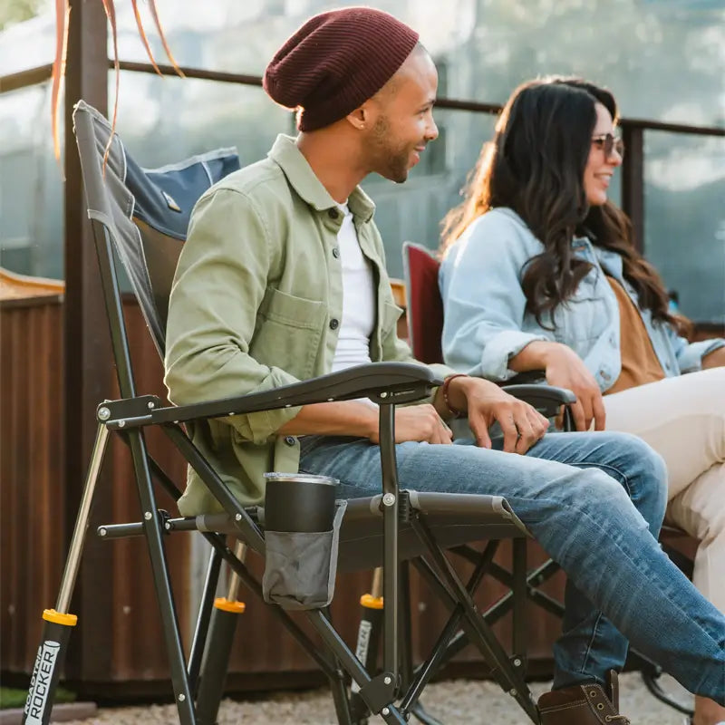 Man seated in a mercury gray RoadTrip Rocker, chatting with a woman outdoors during a relaxed gathering.