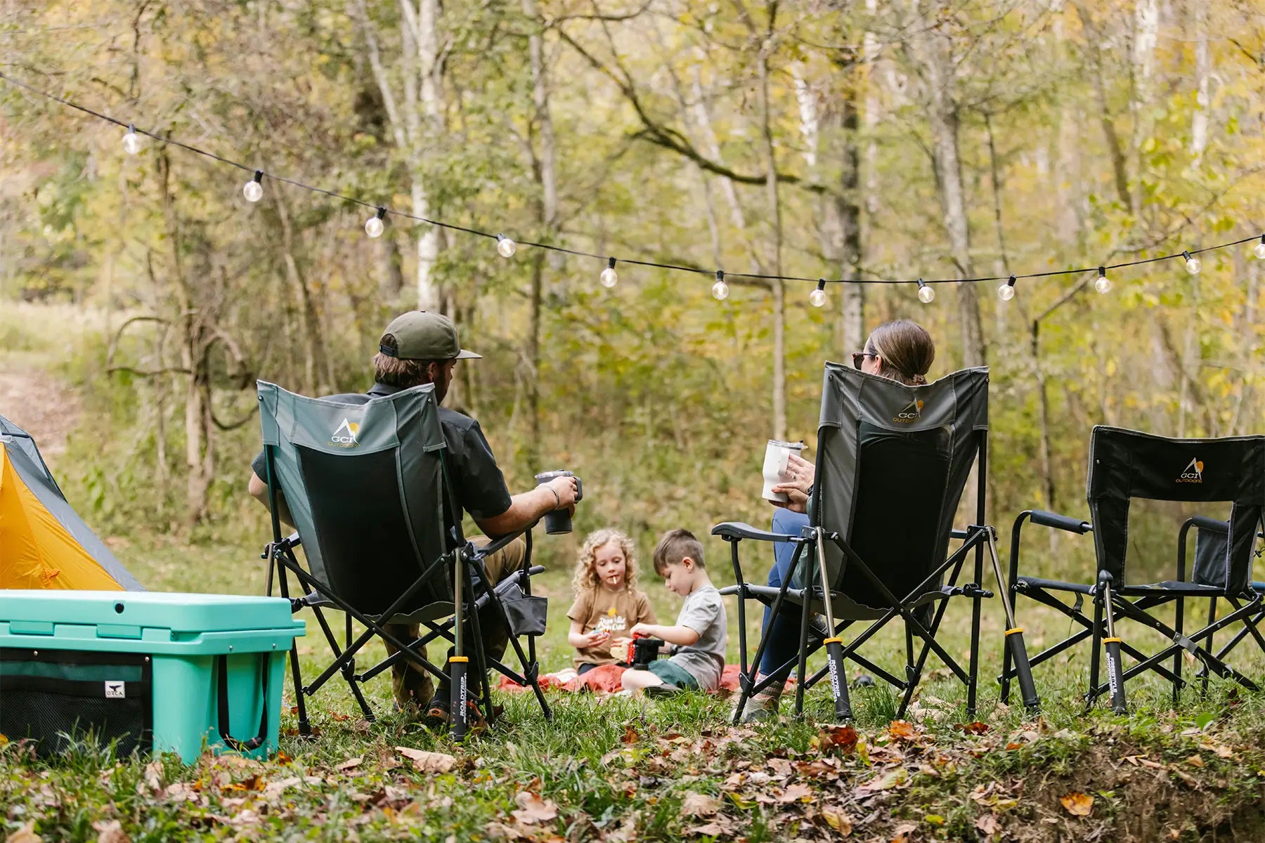 A couple sitting watching their kids play on a blanket while sitting in their roadtrip rocker chairs. 
