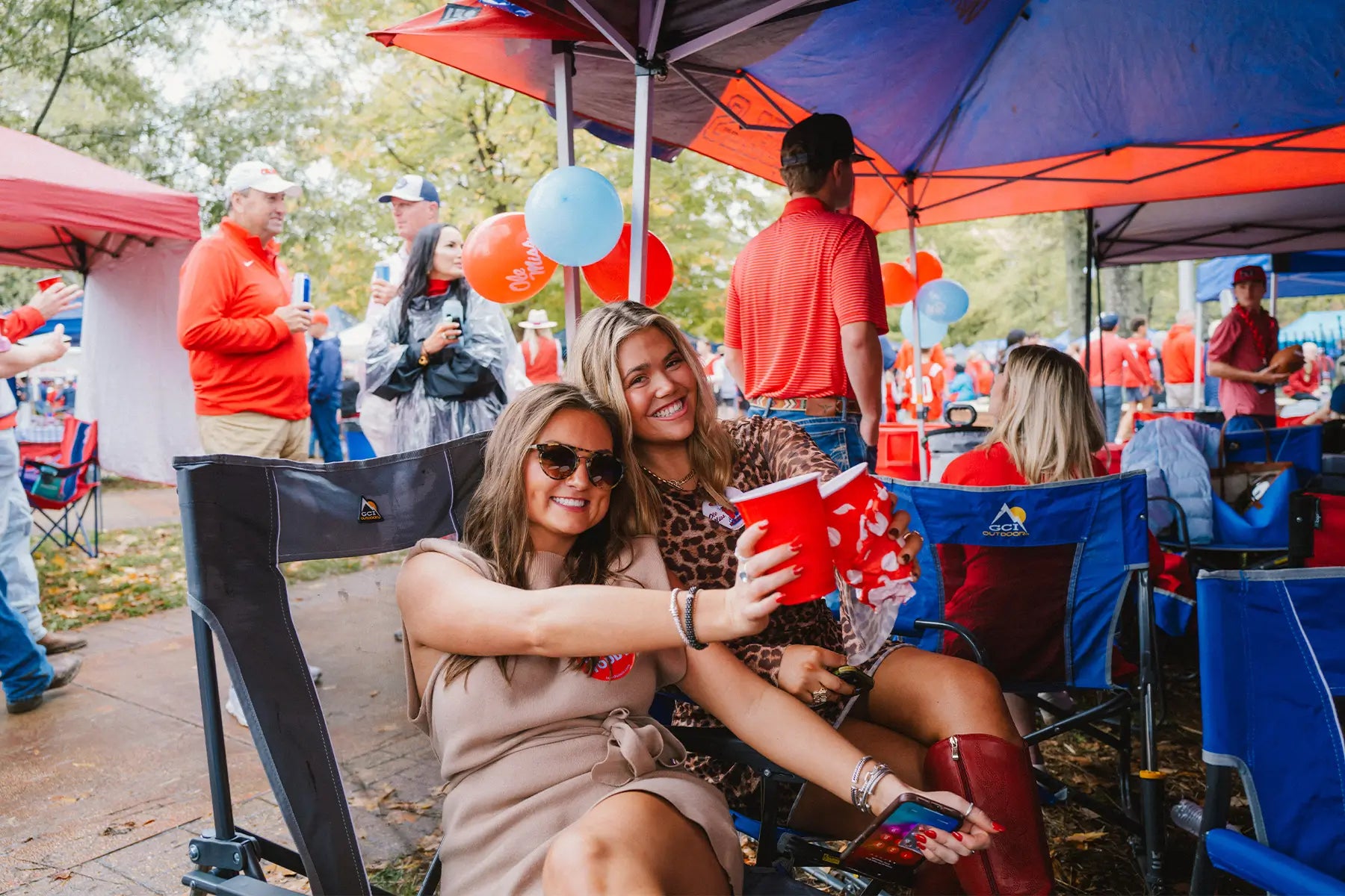 Two ladies sitting in a Roadtrip Rocker while partying at a tailgate. 