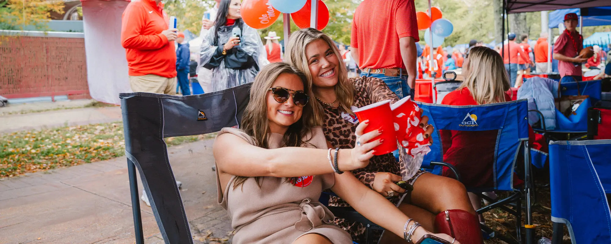 Two ladies sitting in a Roadtrip Rocker while partying at a tailgate. 