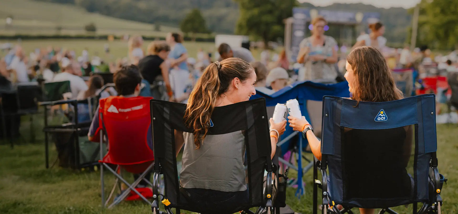 Two women cheering with their drinks at a concert venue while sitting in stowaway rockers. 