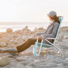 A woman overlooking a body of water while resting in the seafoam Bi-Fold Beach Chair. 