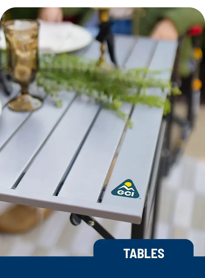 Close-up of a GCI Outdoor Slim-Fold Table with a plant centerpiece and glassware at an outdoor dining setup.