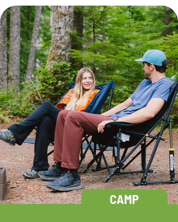 A couple sitting together in two Puff Rocker chairs in a wooded area. 