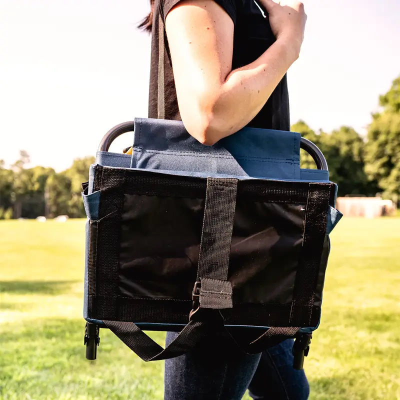Person carrying a folded SitBacker over their shoulder with the strap, walking across a grassy field.