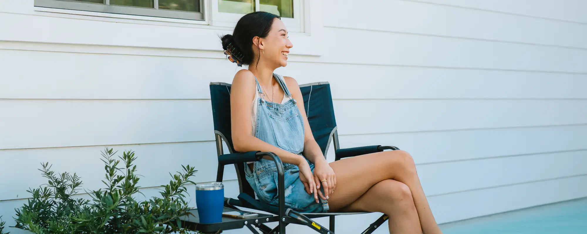 Woman sitting in a Slim-Fold Director’s Chair on a patio, smiling and holding a drink.