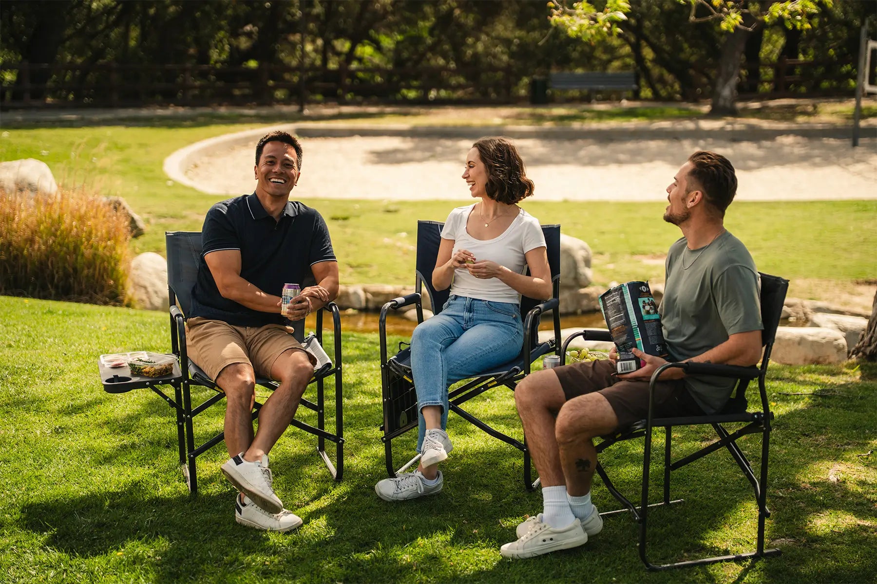 A group of people eating snacks at a park while sitting in their Slim Fold Director XL chair. 