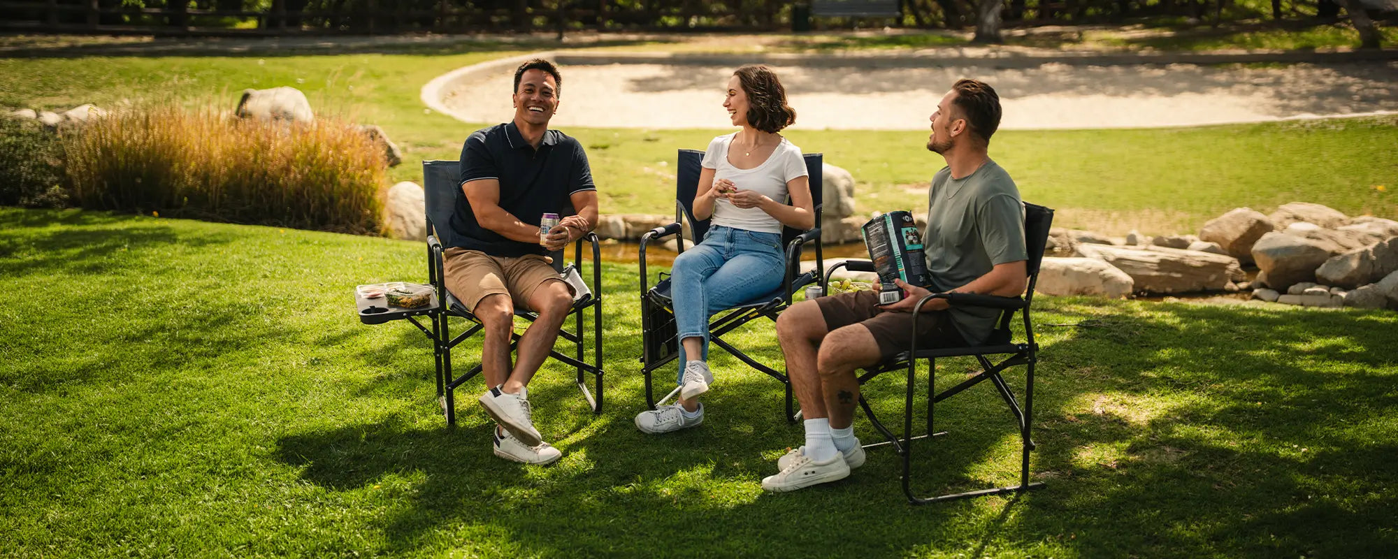 A group of people eating snacks at a park while sitting in their Slim Fold Director XL chair. 