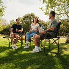 A group of people sitting at a park in their Slim-Fold Directors Chair XL. 