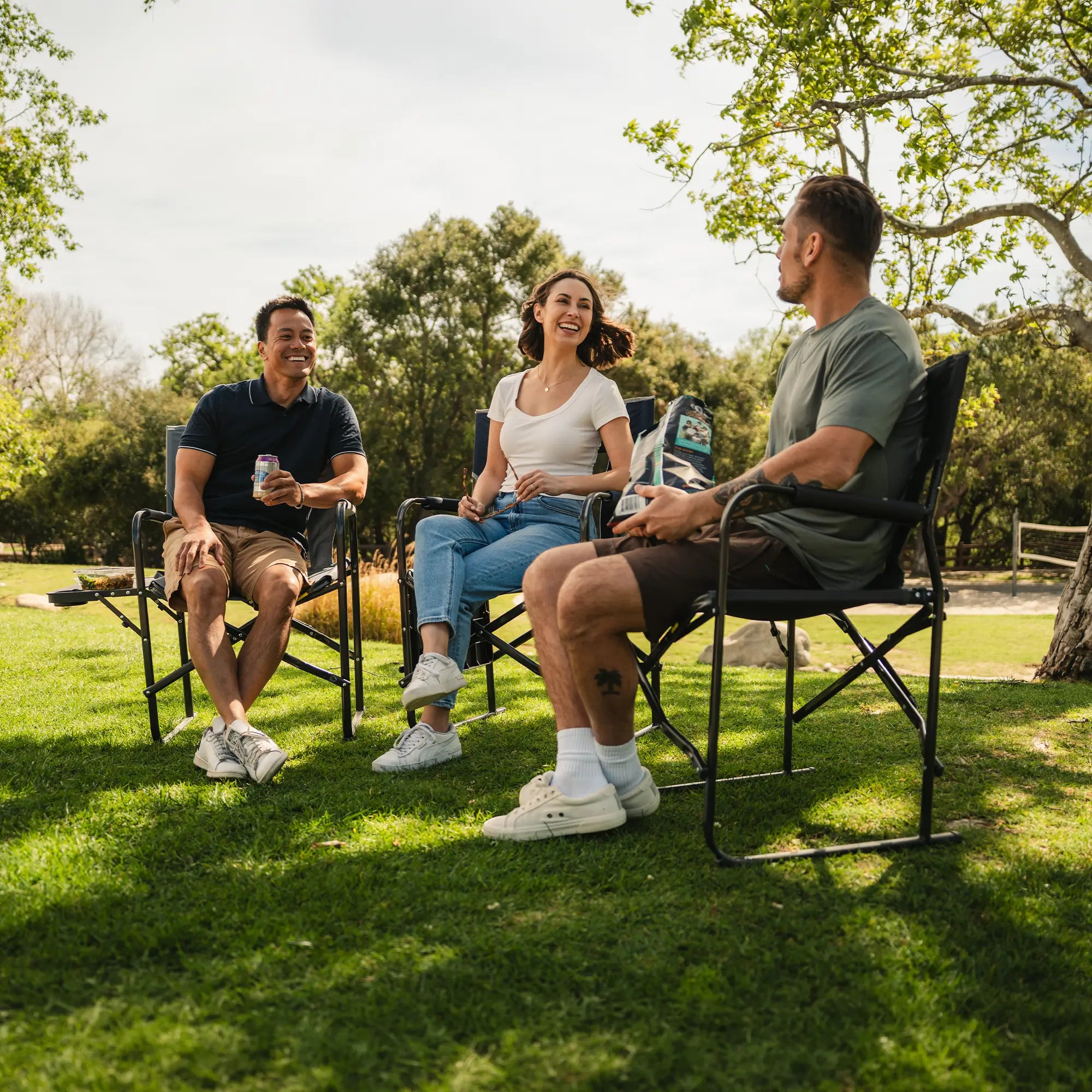 A group of people sitting at a park in their Slim-Fold Directors Chair XL. 