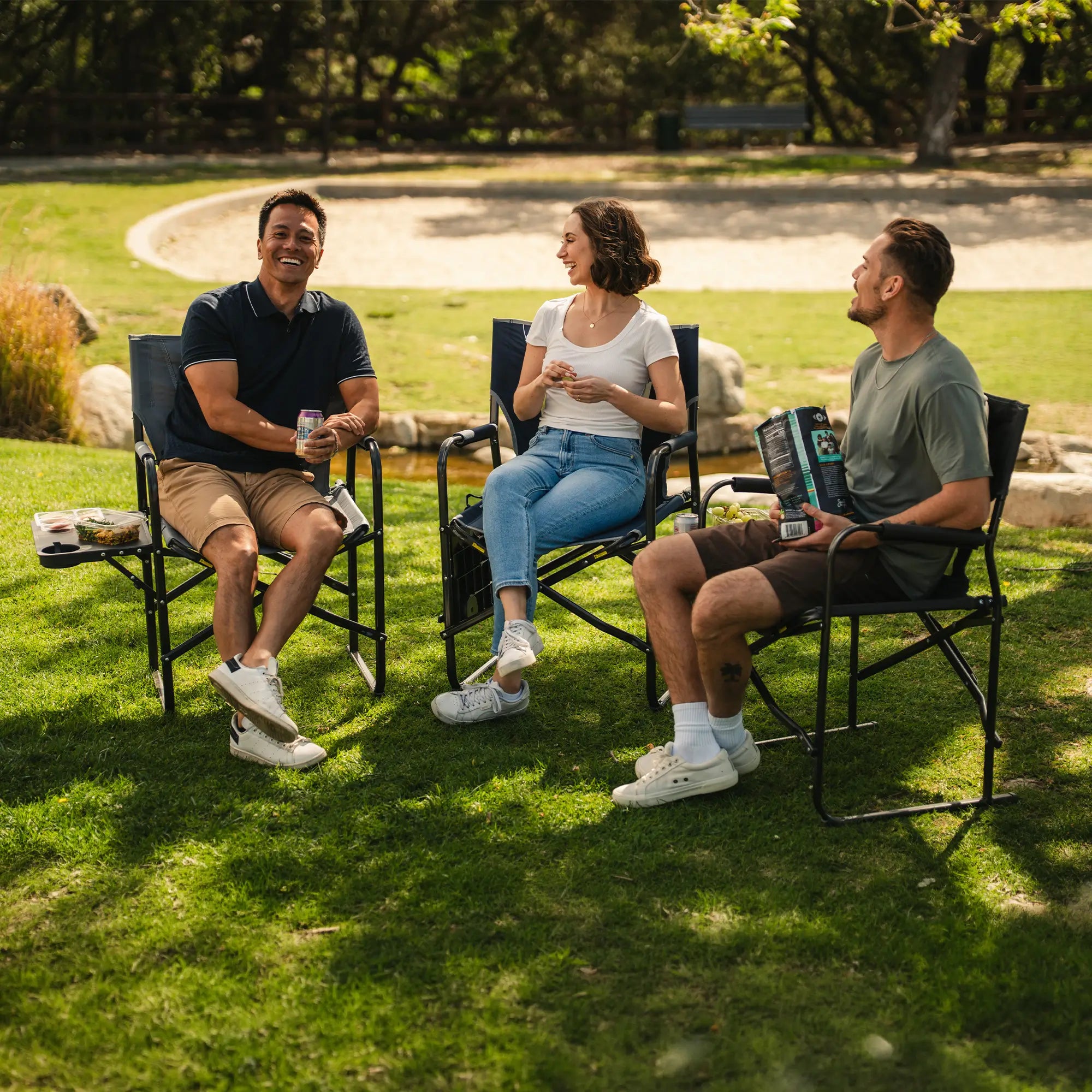 A group of people sitting at a park in their Slim-Fold Directors Chair XL. 