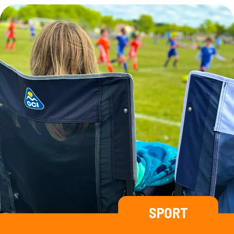 Person sitting in a black Stowaway Rocker chair watching a soccer game, with a blanket draped over the back.